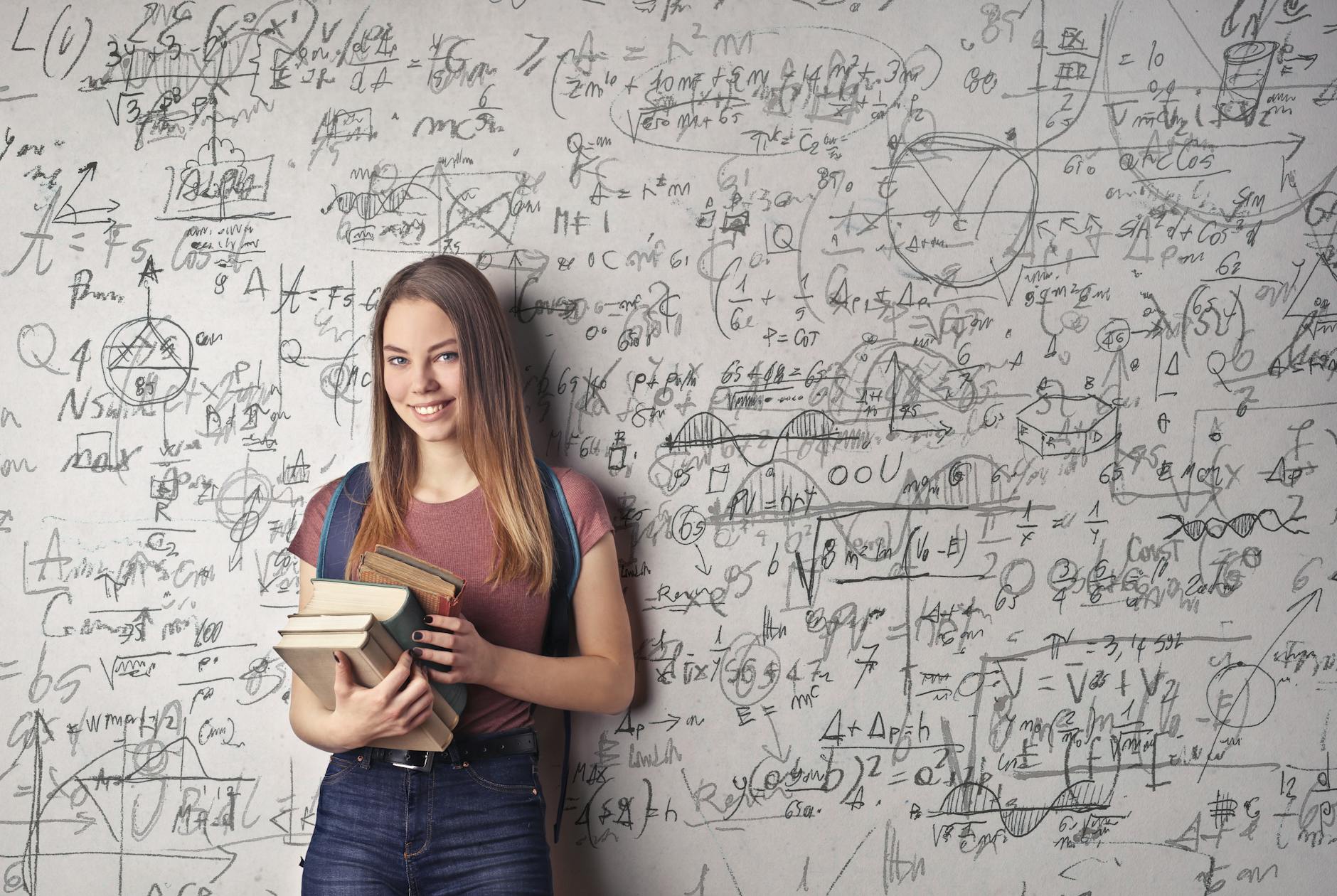 A woman standing in front of a blackboard full of physics formulas.