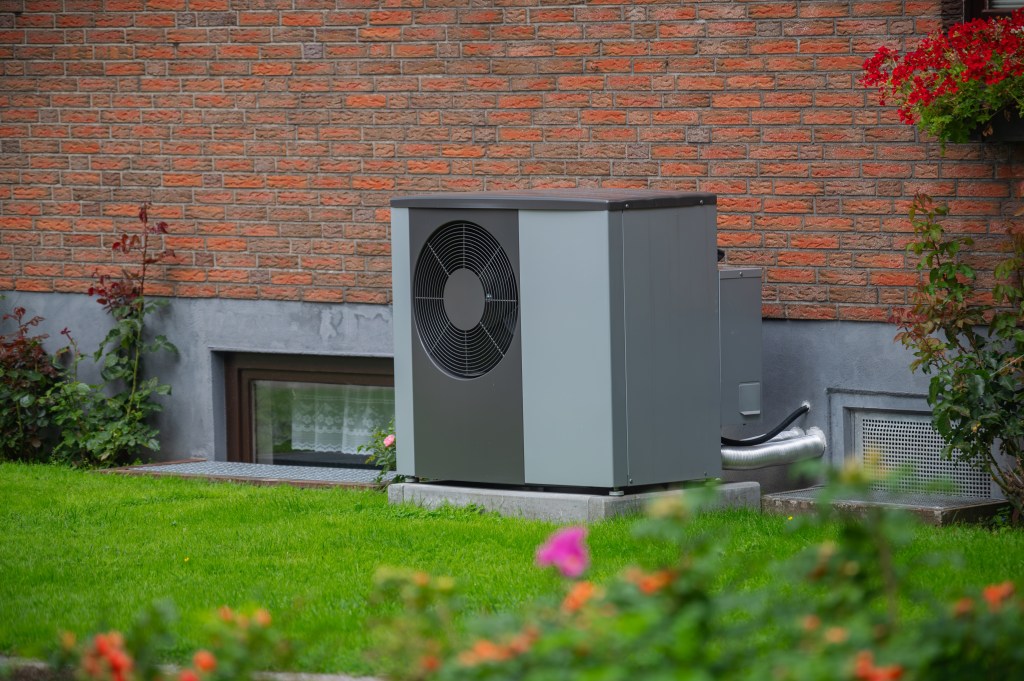 Grey heat pump standing towards the wall of an old red brick house.