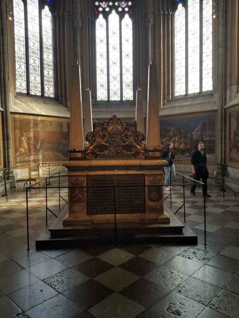 Heavily decorated coffin shaped tomb placed in a large, decorated room filled with paintings.