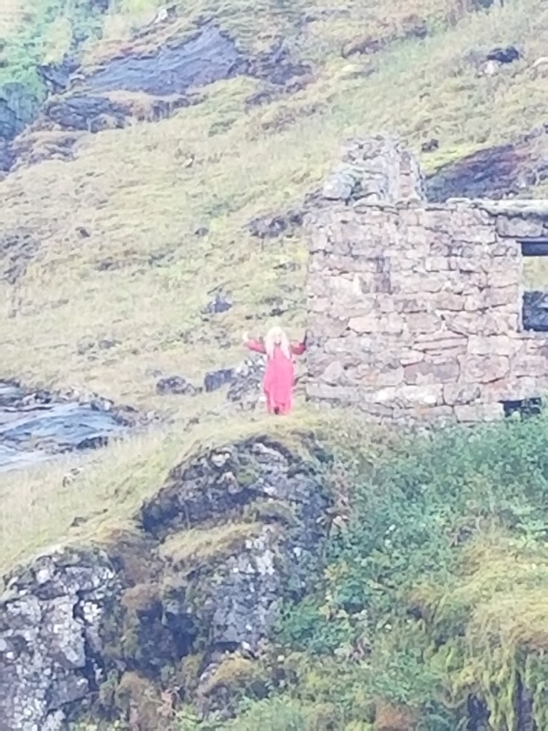A Huldra dressed in red standing on a mountain side | Scandinavian Folklore