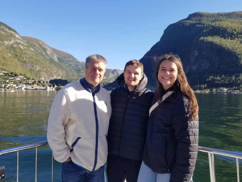 Three people standing on a boat on the fjord.