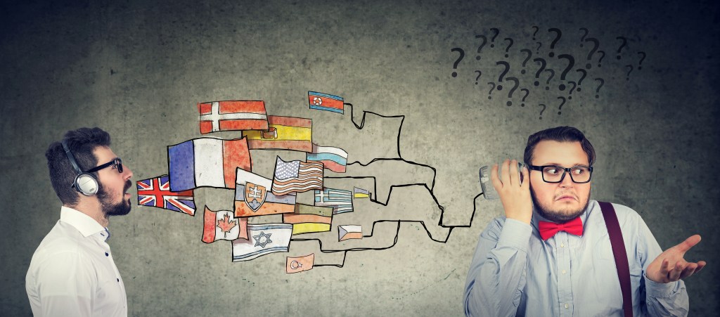 On the left, a business guy speaking a whole bunch of languages indicated by flags coming out of his mouth. On the right another businessman surrounded by question marks | Accents are very difficult to lose