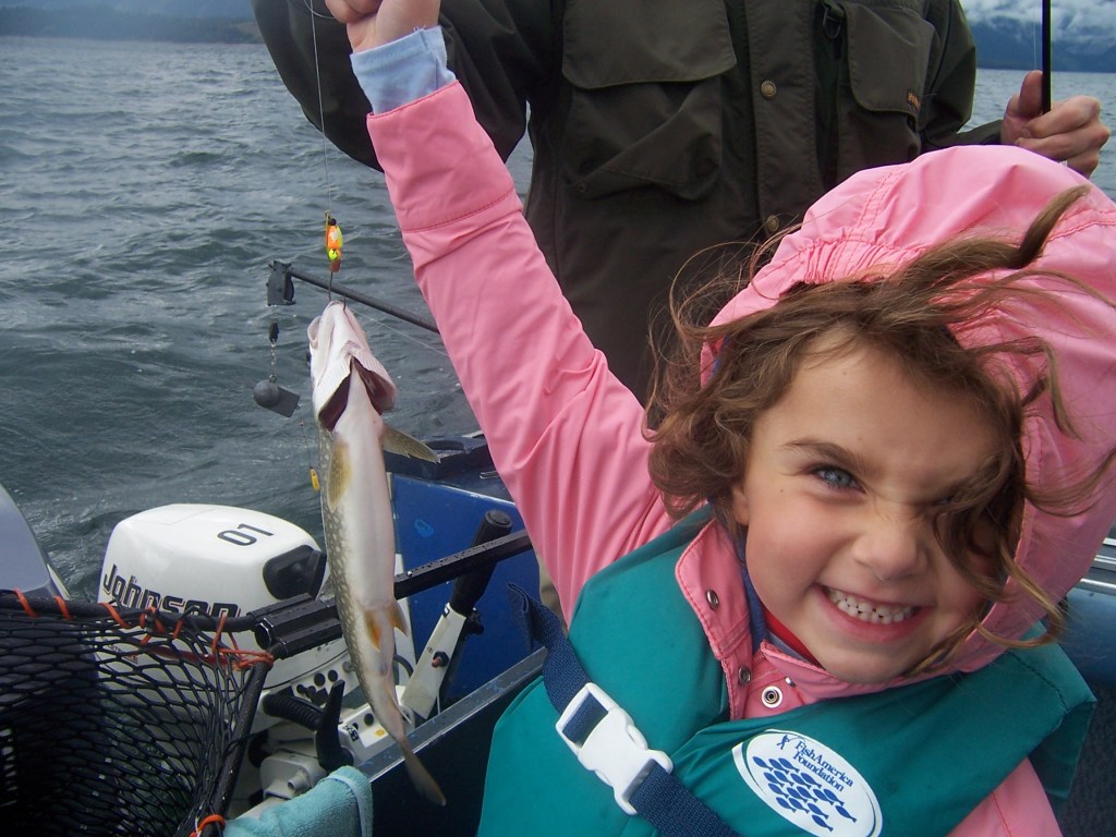 My daughter is wearing a pink rain jacket. She is holding a rainbow trout.