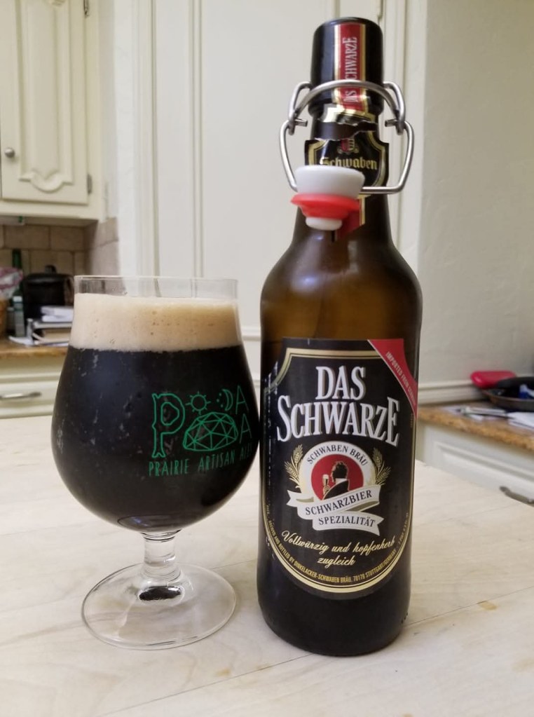 On the left, glass with black beer. It has a mocha-colored head. On the right is the bottle. The label says Das Schwarze.