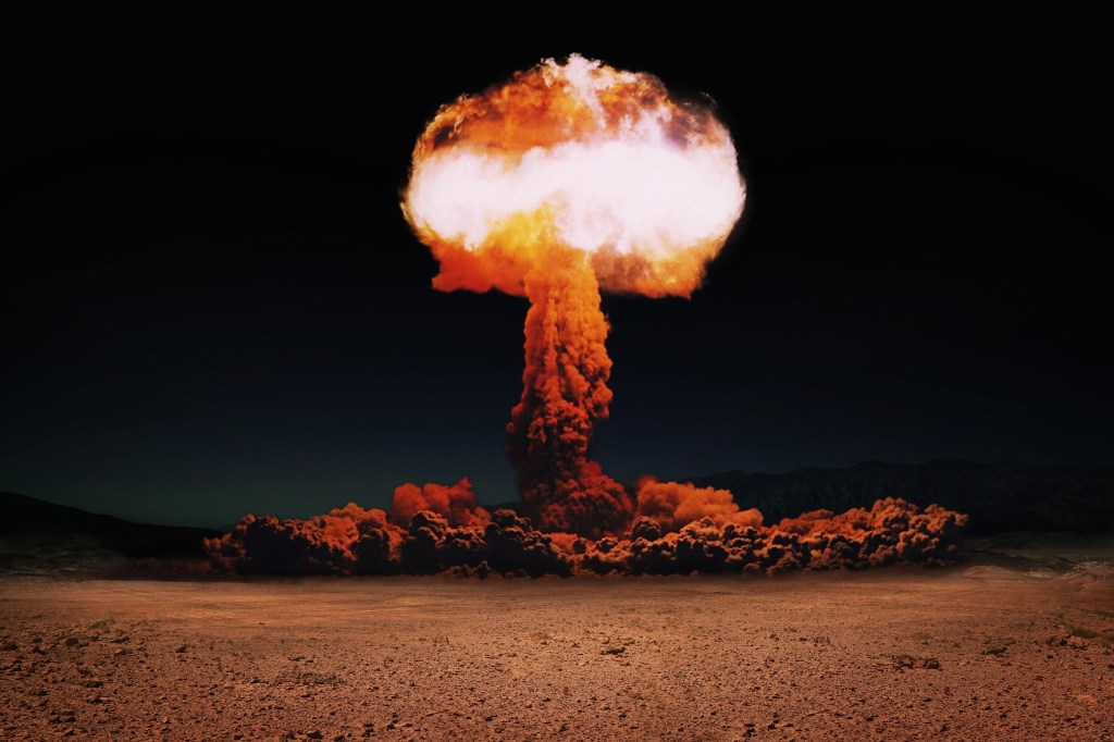 An enormous nuclear bomb explosion in the dessert featuring a huge mushroom cloud.