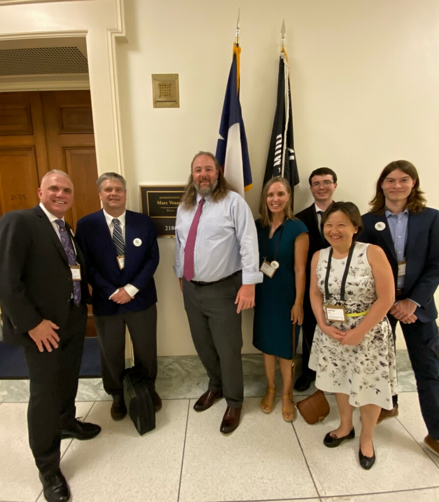 A photo of seven people standing in front of Representative Marc Veasey’s Office. The legislative aide, Mike Burnside, is standing in the middle. There is also a Texas flag.