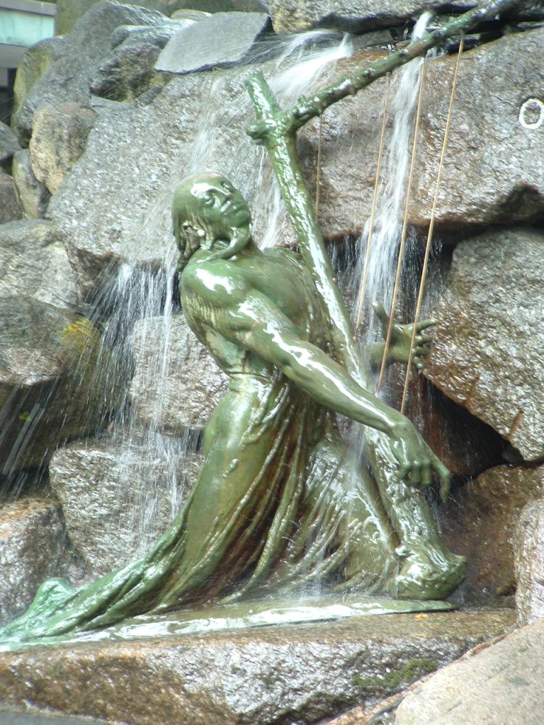 Greenish statue of Fossegrim standing in a small waterfall playing a harp. | Scandinavian Mythology