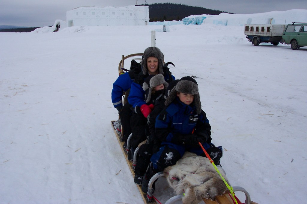 My wife and three children are sitting on a dog sled and looking into the camera.