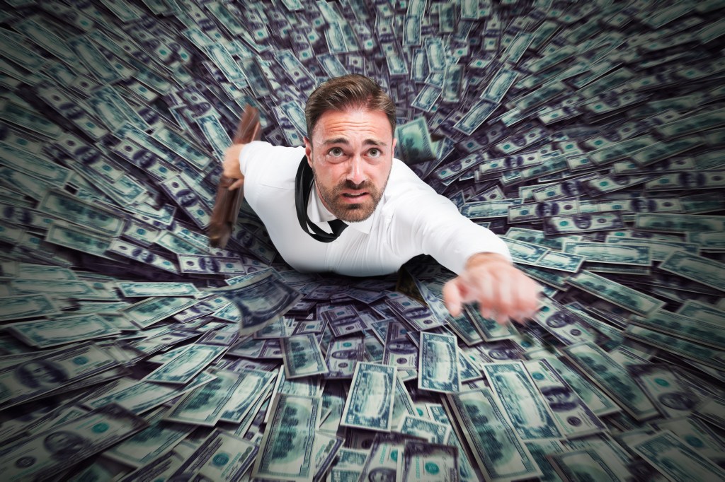 A man is being sucked into a hole filled with money.