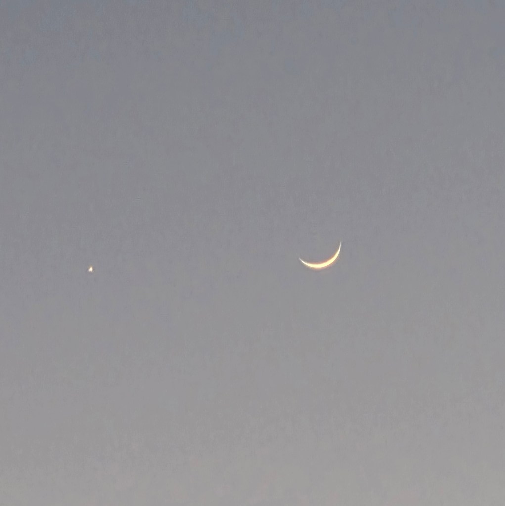It is a dark photo with a bright dot on the left and the moon crescent on the right.