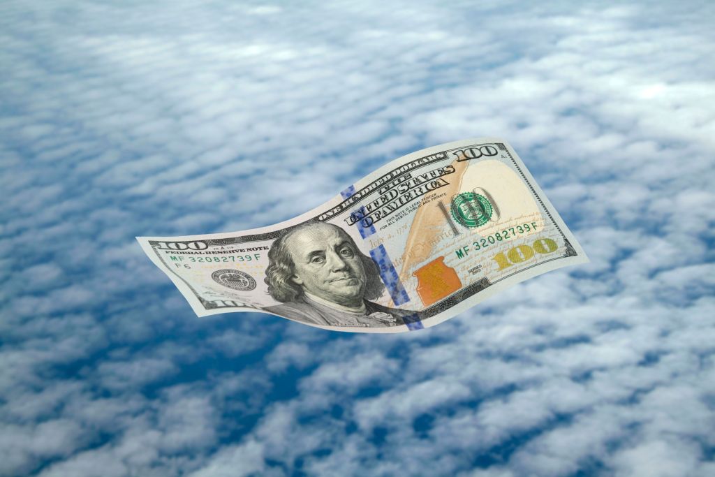 A one hundred US Dollar bill sailing through a cloudy sky.