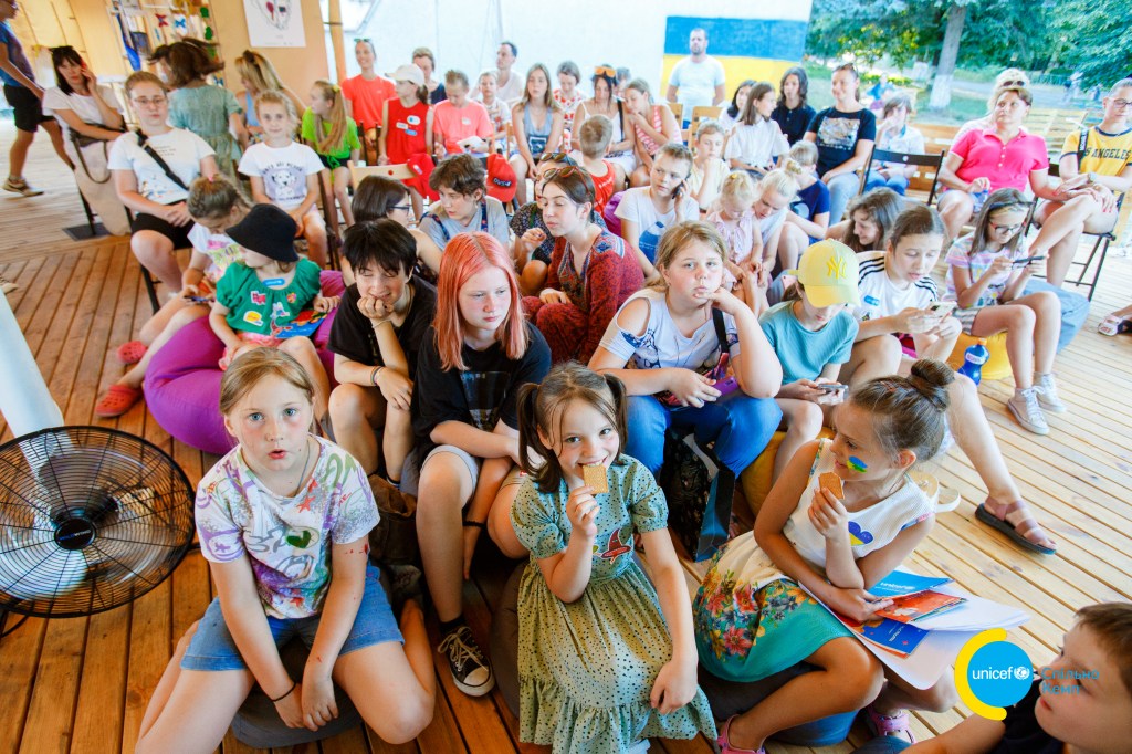 A large number of Ukrianian school children sitting on a patio.